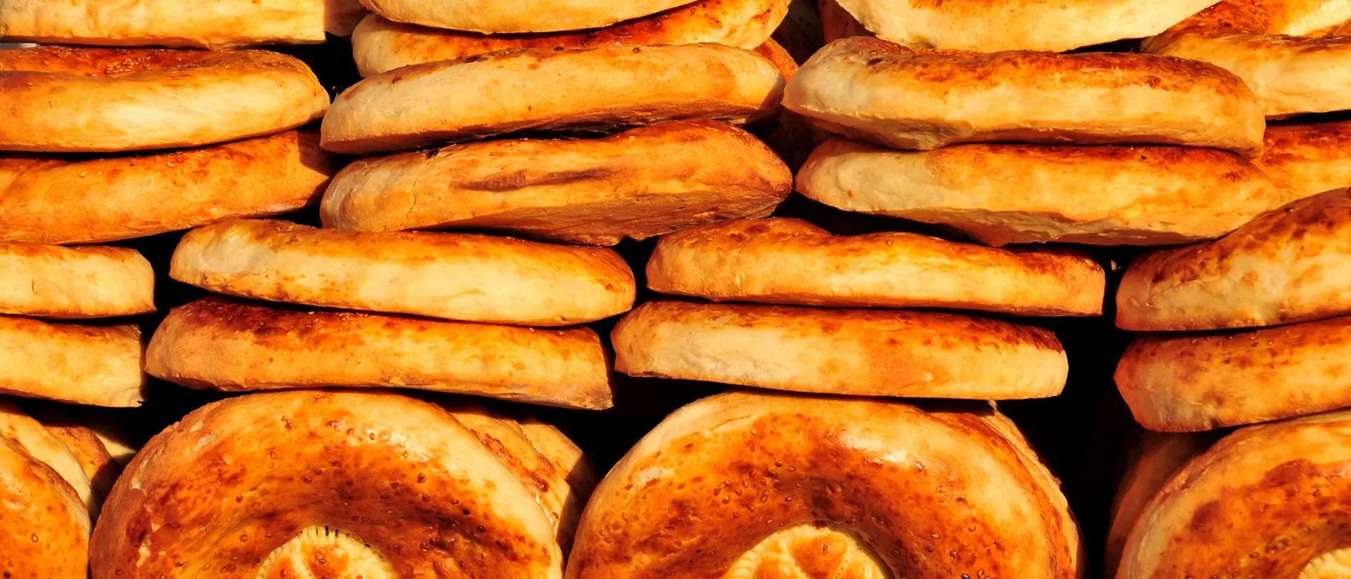 A stack of freshly baked round bread, golden brown with a slightly crisp surface and a decorative pattern on top.