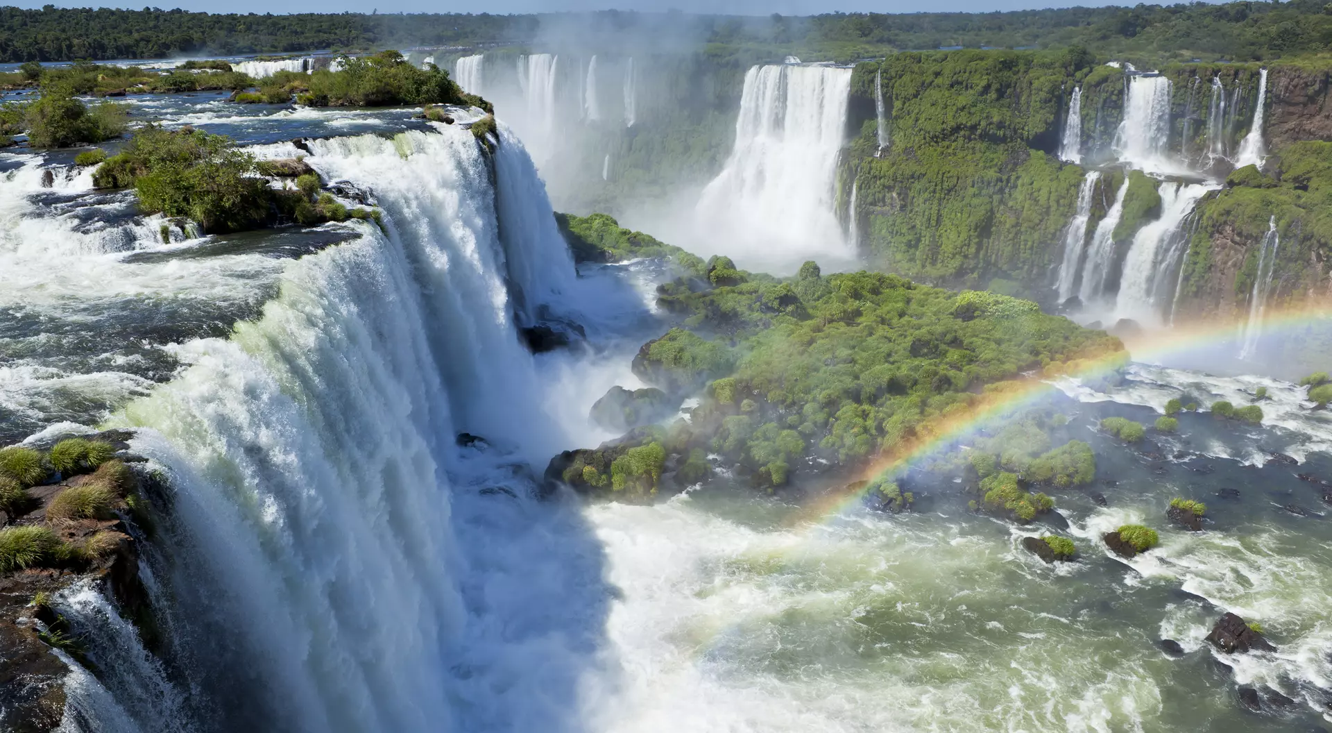 A stunning view of waterfalls surrounded by greenery, with a rainbow arching over the mist.