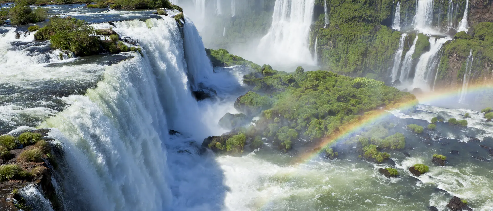 A stunning view of waterfalls surrounded by greenery, with a rainbow arching over the mist.
