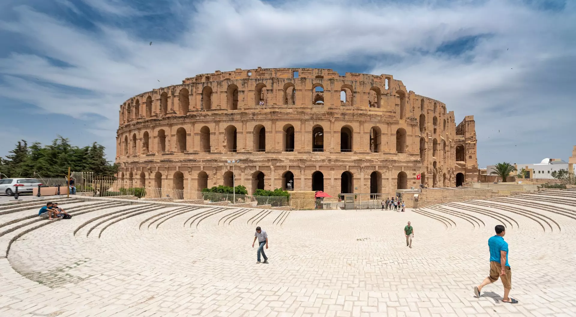 The ancient Roman amphitheater stands tall under a blue sky, surrounded by visitors on a sunny day.