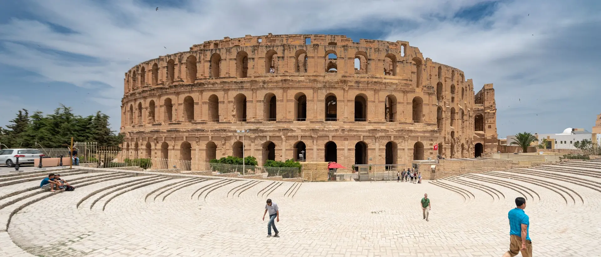 The ancient Roman amphitheater stands tall under a blue sky, surrounded by visitors on a sunny day.