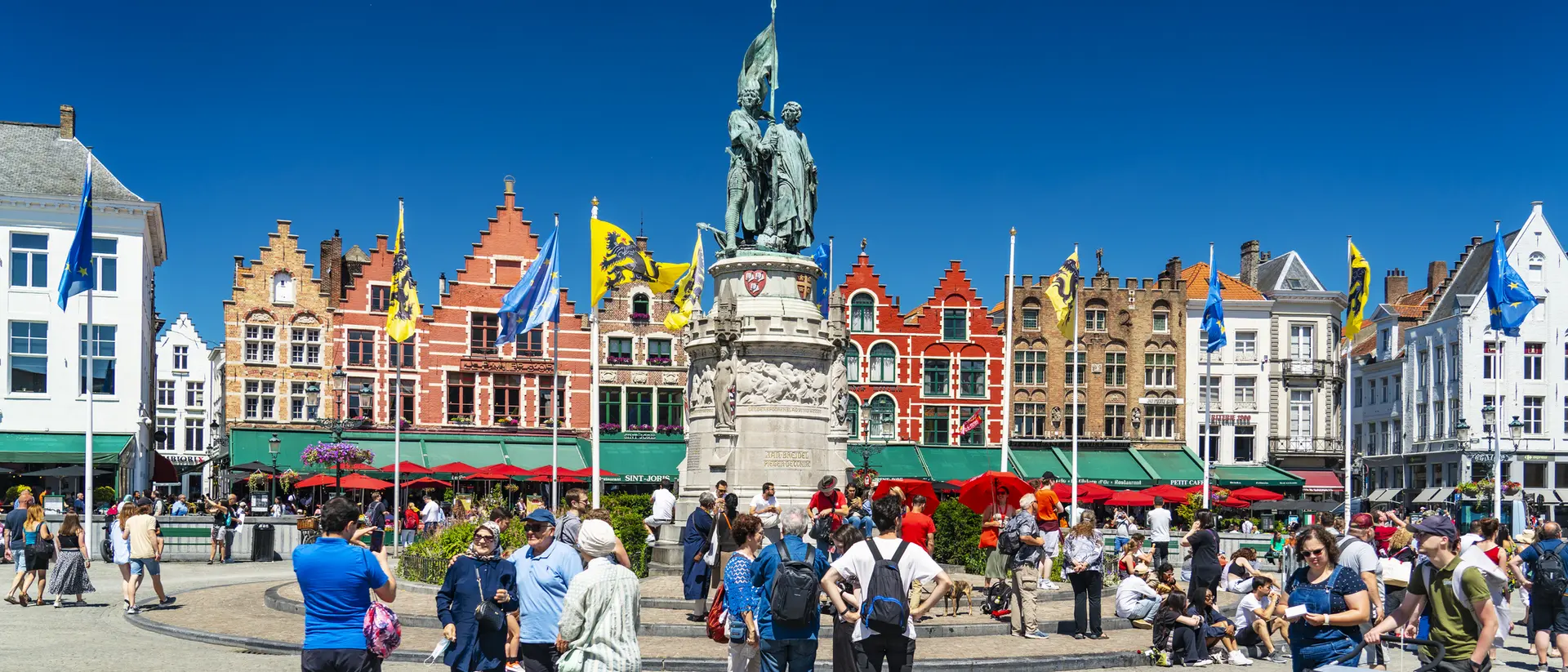 A busy square with a statue in the center, surrounded by colorful buildings and a crowd of people enjoying the day.
