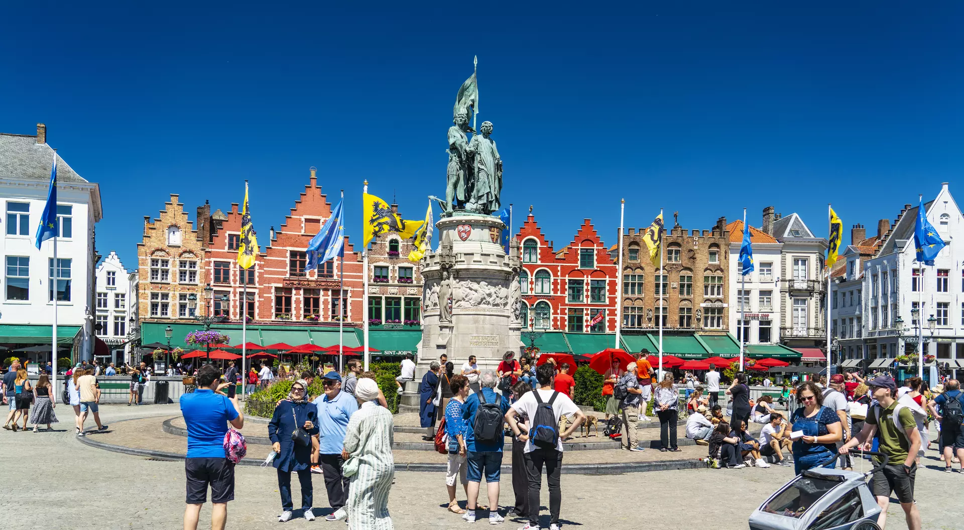 A busy square with a statue in the center, surrounded by colorful buildings and a crowd of people enjoying the day.