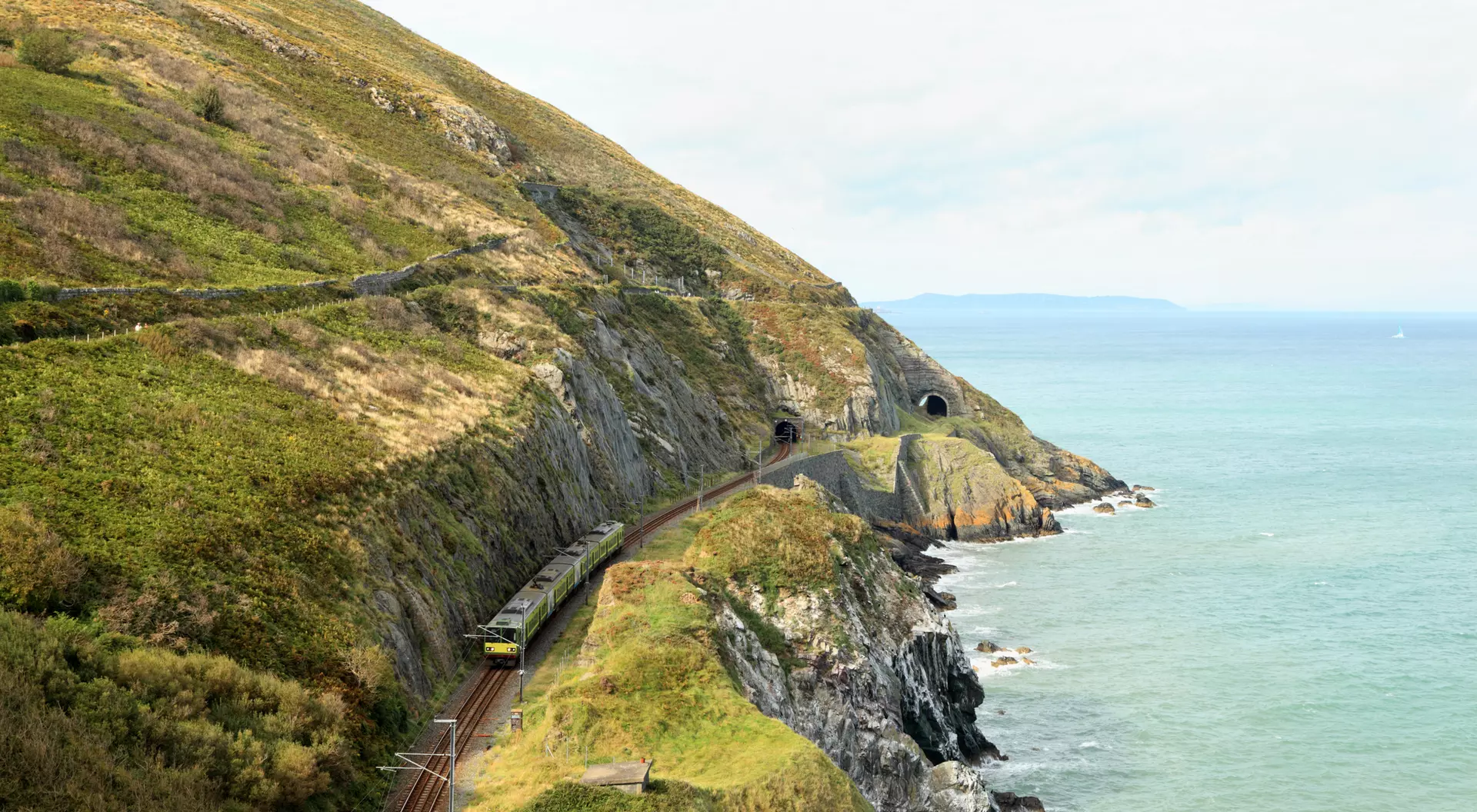Train running along a coastal track with hills and tunnels on one side and the sea on the other.