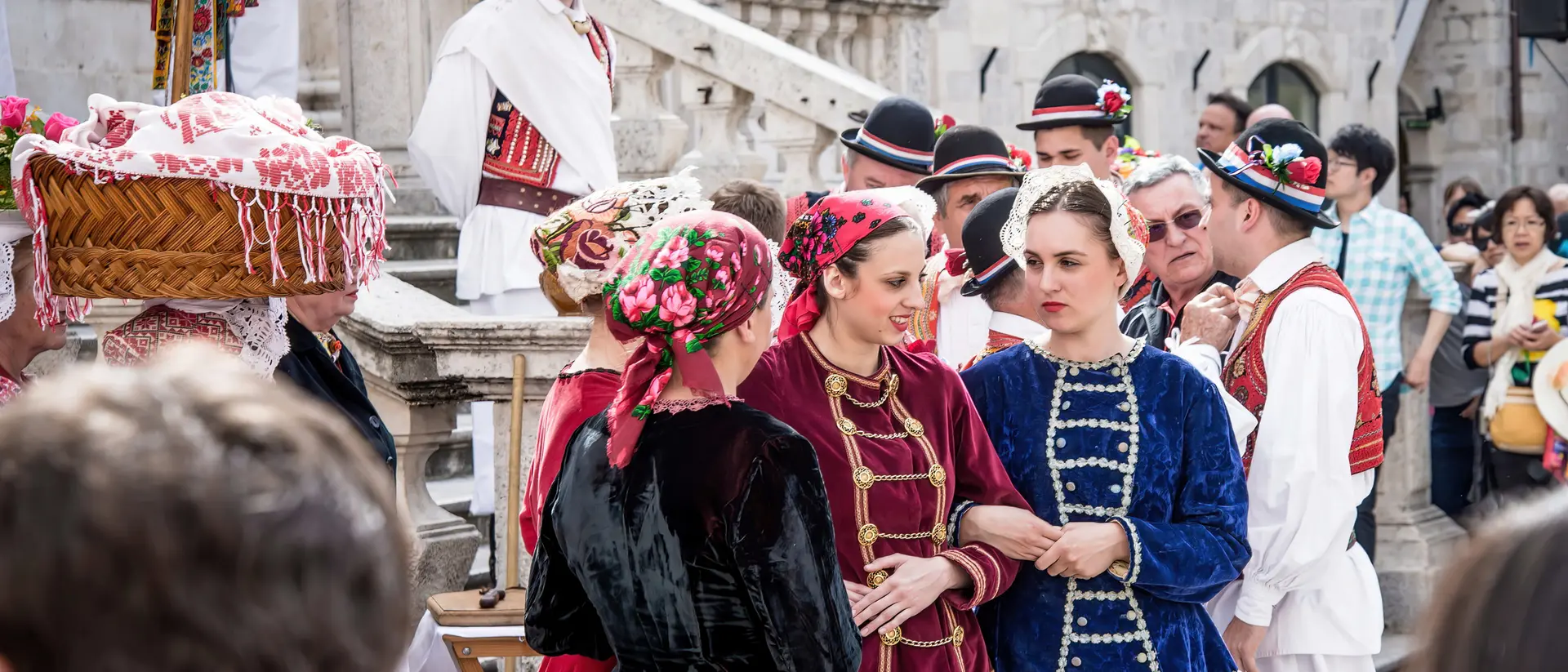 Group of people in traditional costumes at a cultural event, engaged in conversation, with a festive atmosphere.