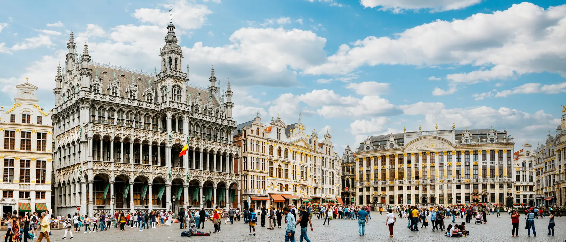 A bustling city square in Brussels, featuring historic buildings under a bright, partly cloudy sky.