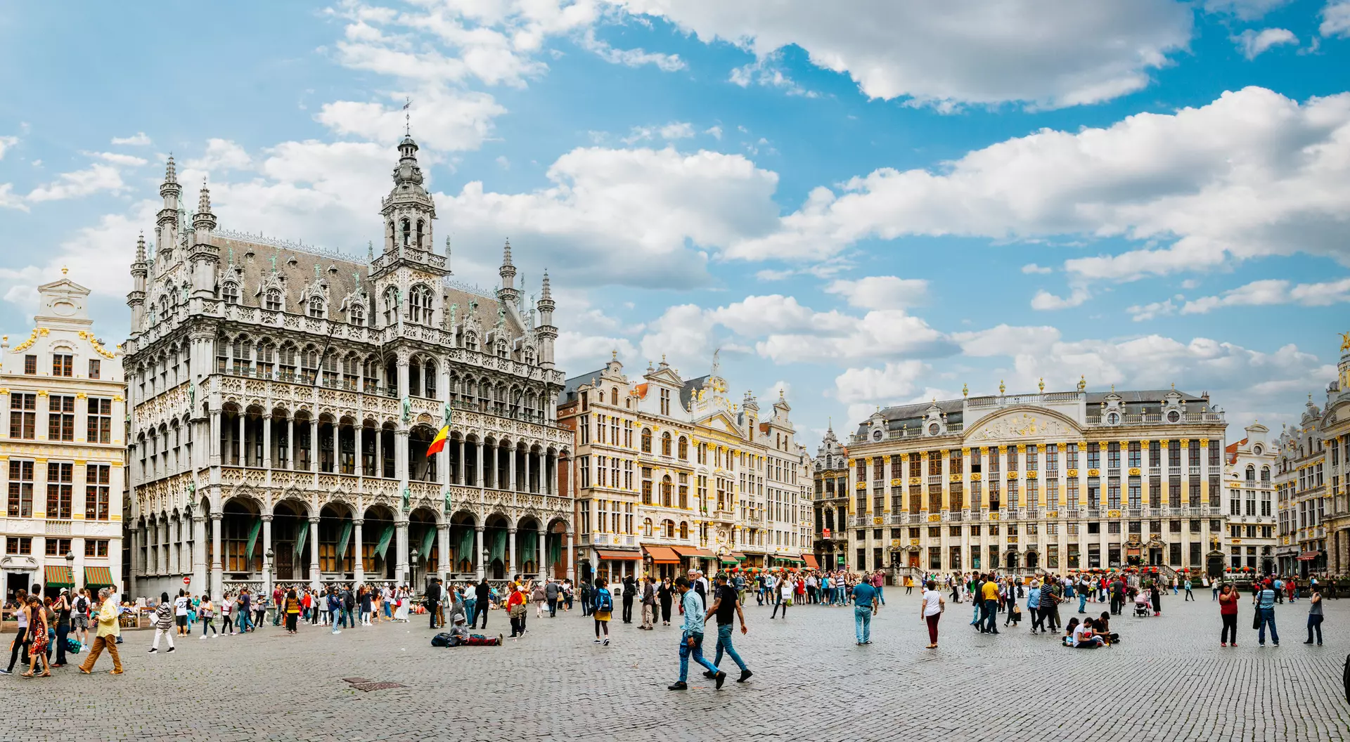 A bustling city square in Brussels, featuring historic buildings under a bright, partly cloudy sky.