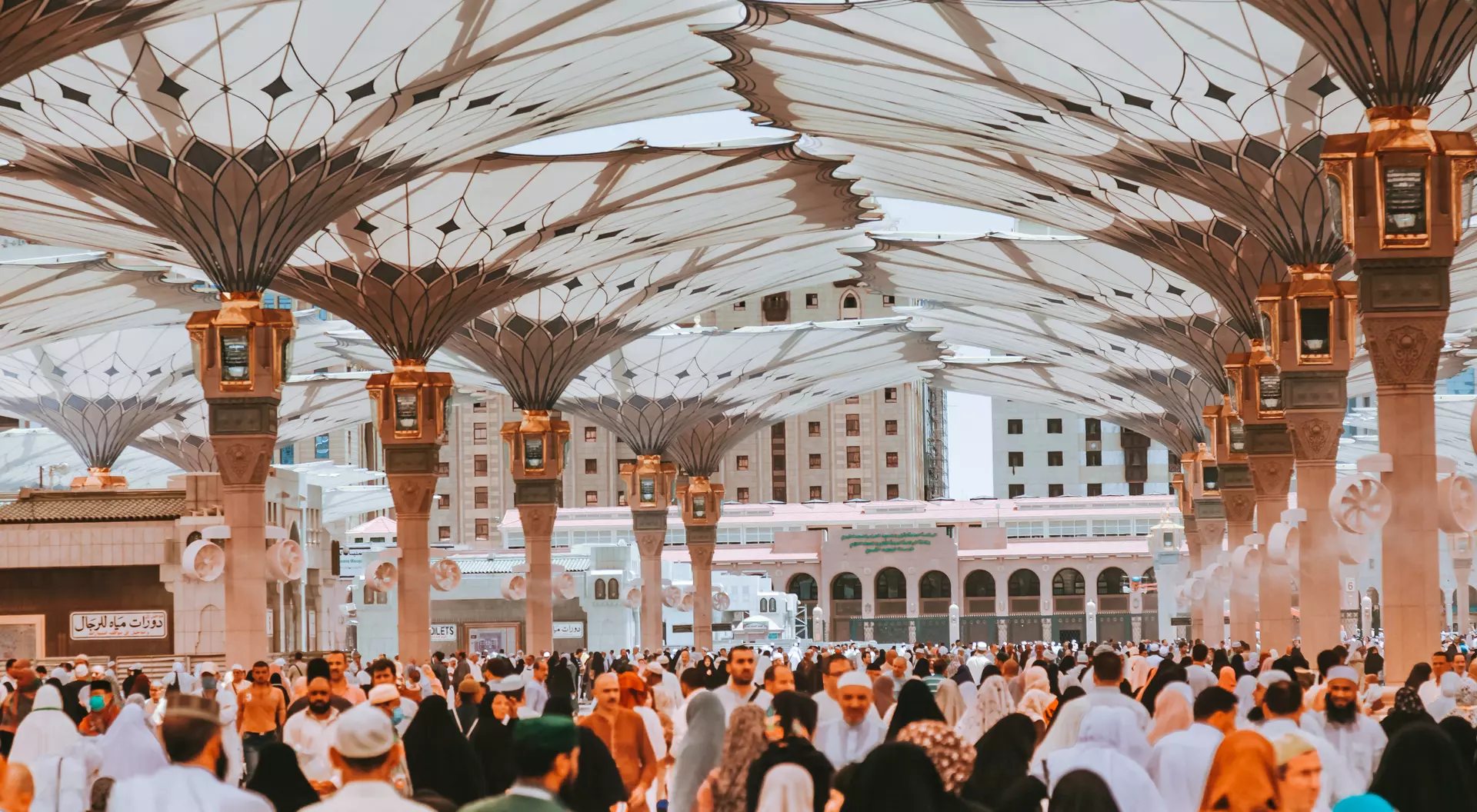 A large crowd of people in traditional attire gathers under elaborate canopies at a religious site.