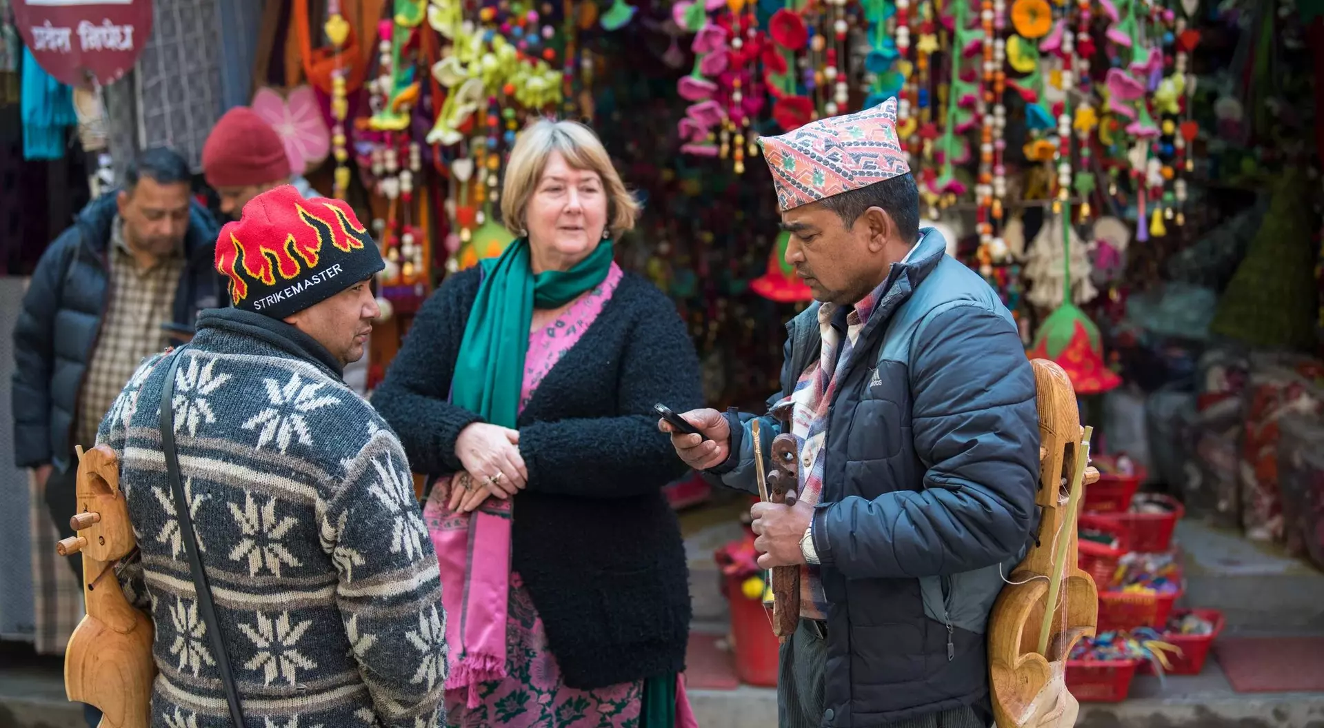 A woman chats with two men in a colorful market, surrounded by vibrant decorations and busy stalls.