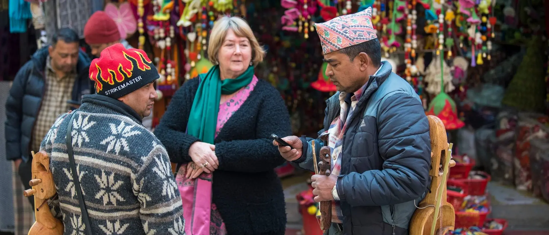 A woman chats with two men in a colorful market, surrounded by vibrant decorations and busy stalls.