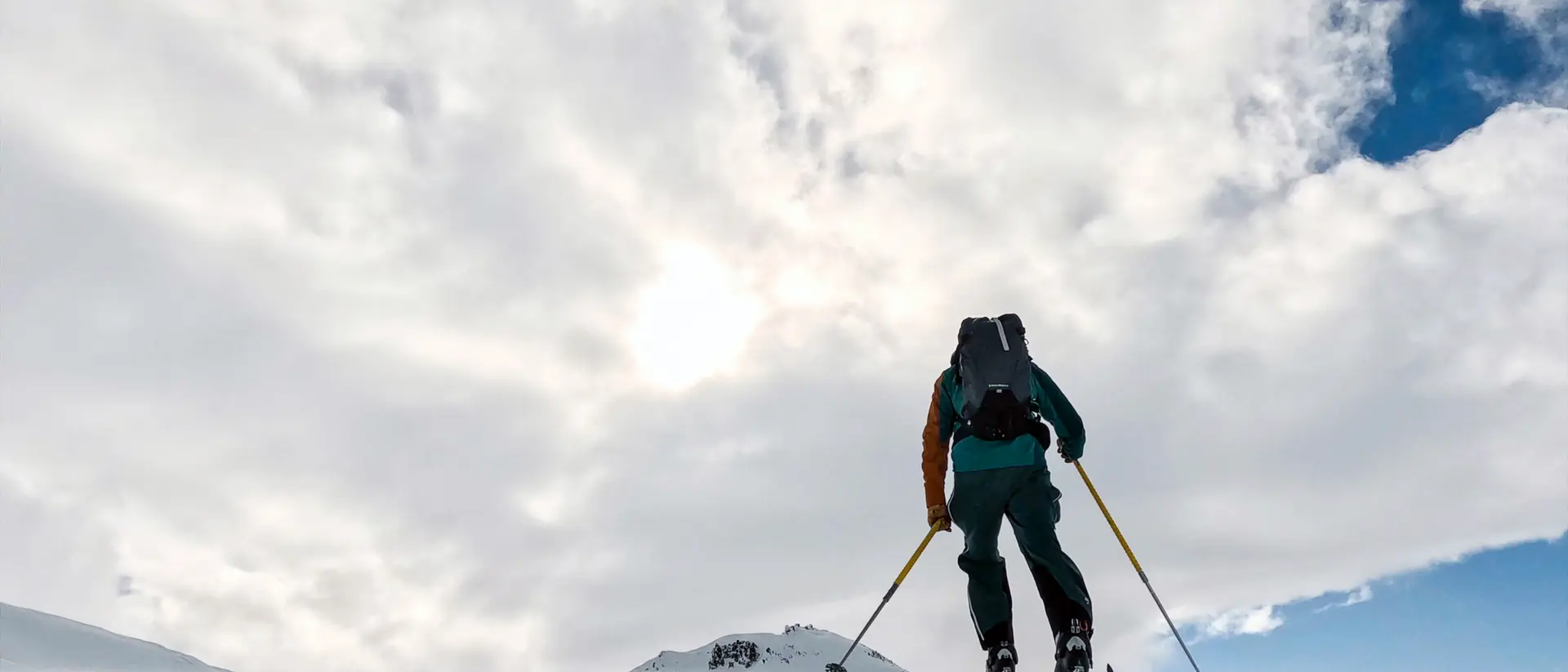 A person skiing uphill in a snowy landscape under a cloudy sky.