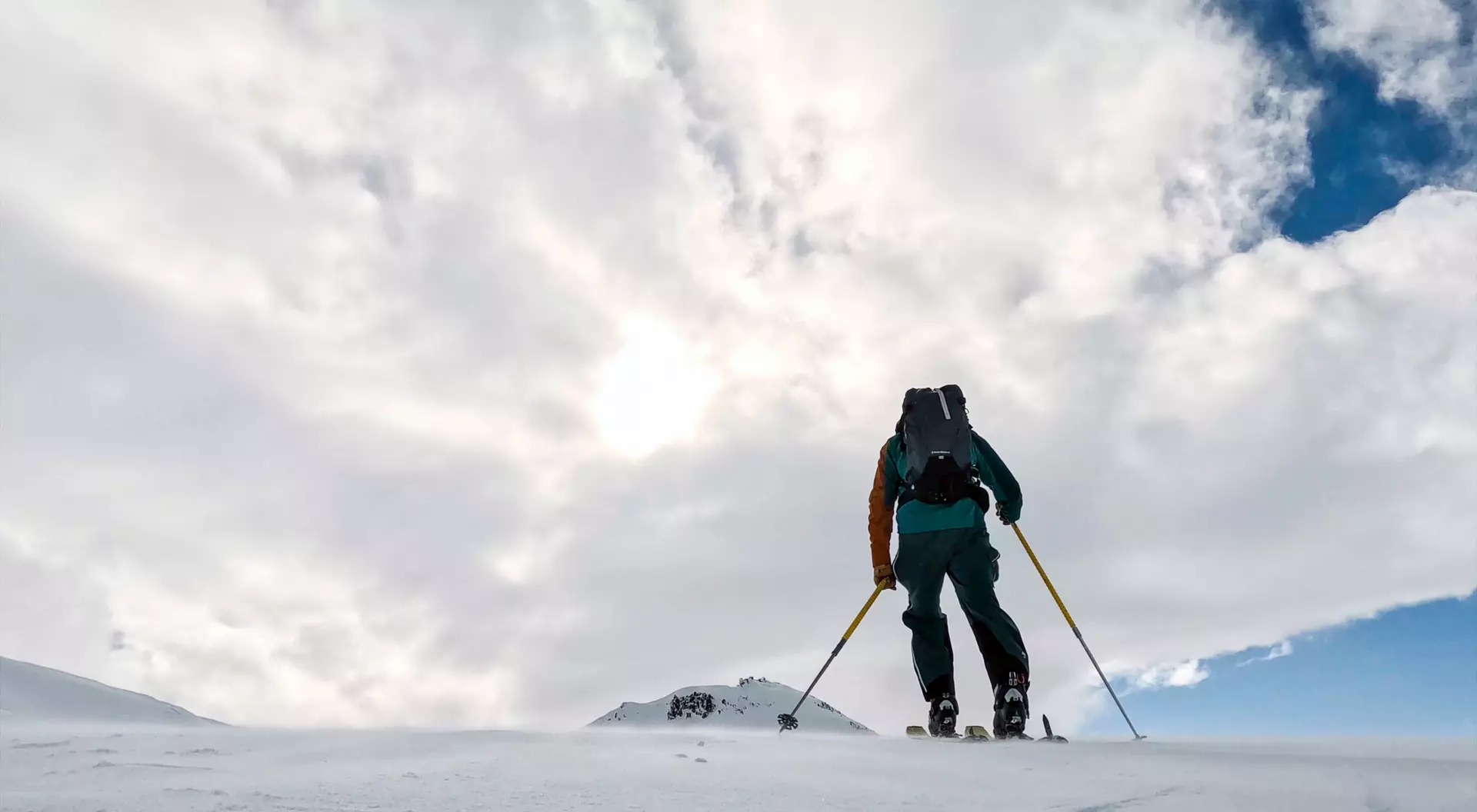 A person skiing uphill in a snowy landscape under a cloudy sky.