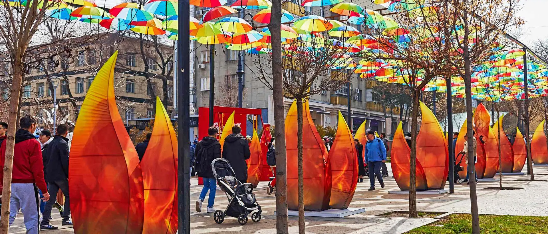 People walk under colorful umbrellas with large flame-shaped art installations lining the path.