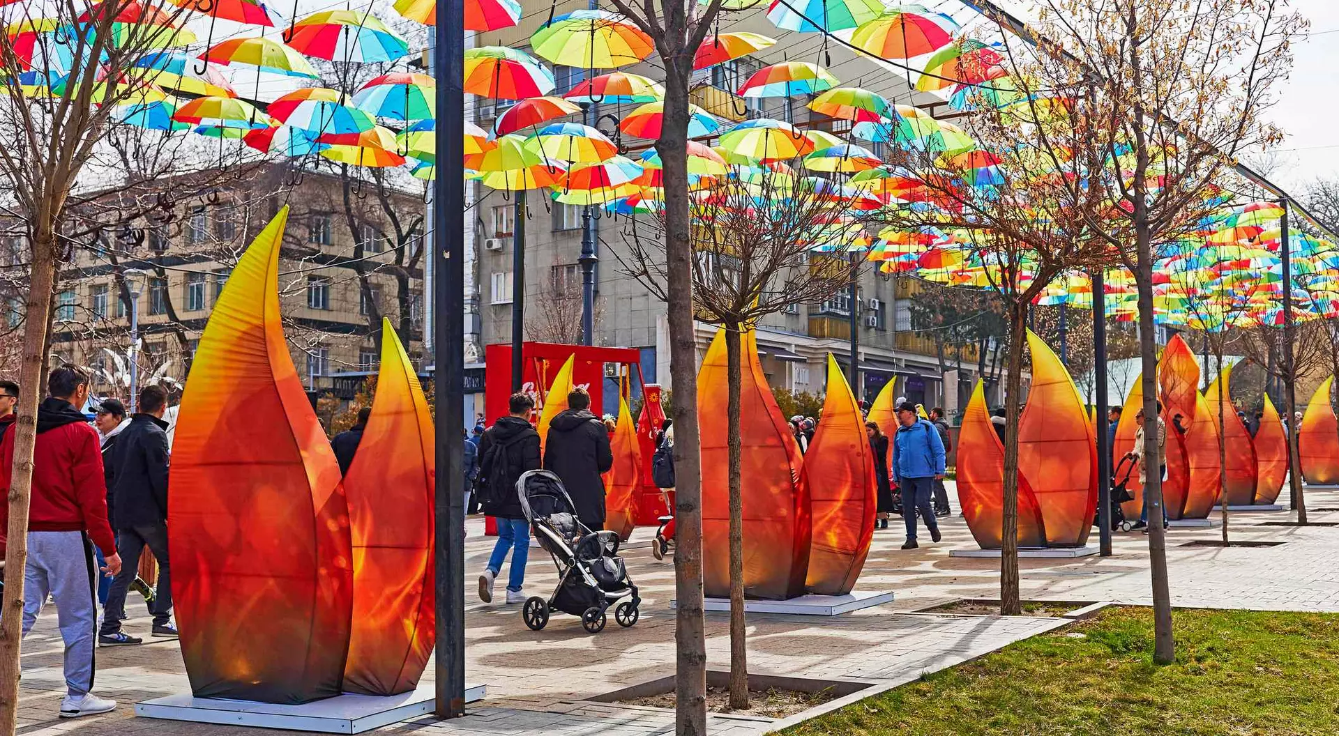 People walk under colorful umbrellas with large flame-shaped art installations lining the path.