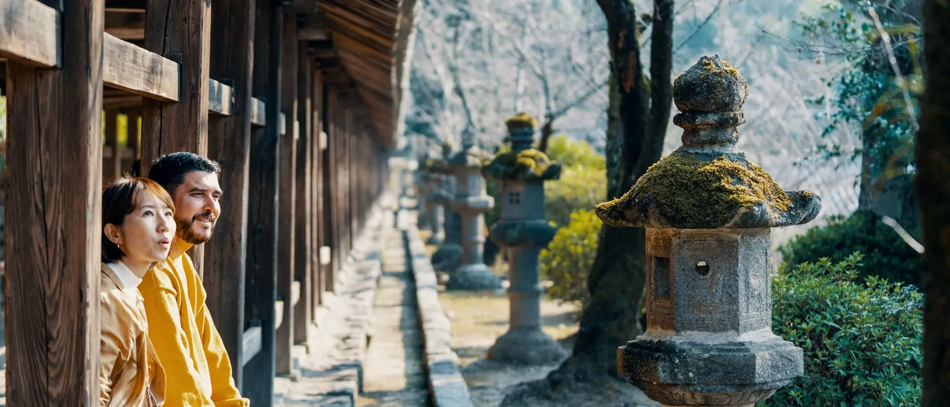 A man and woman sit peacefully on a bench, surrounded by traditional stone lanterns in a serene garden.