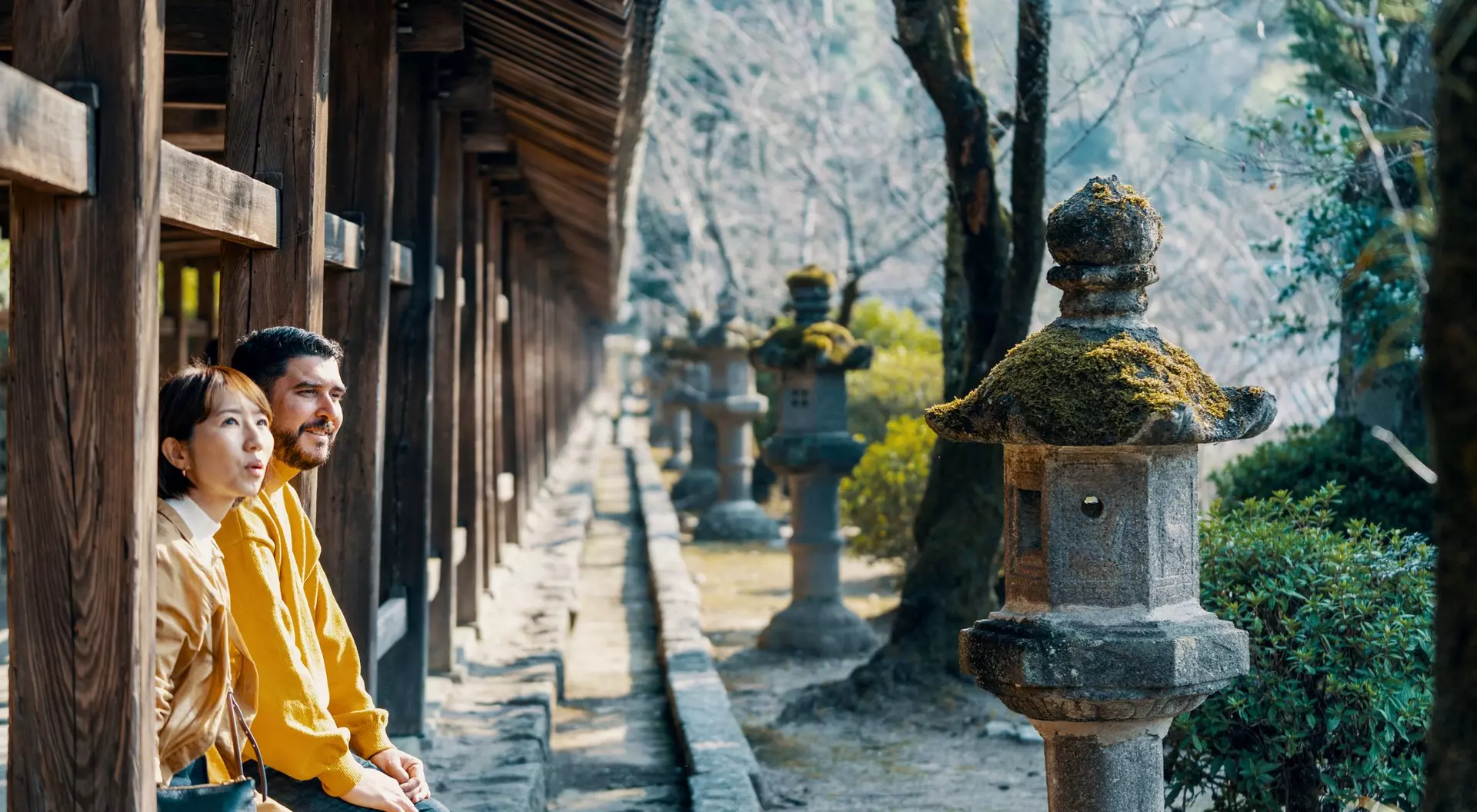 A man and woman sit peacefully on a bench, surrounded by traditional stone lanterns in a serene garden.