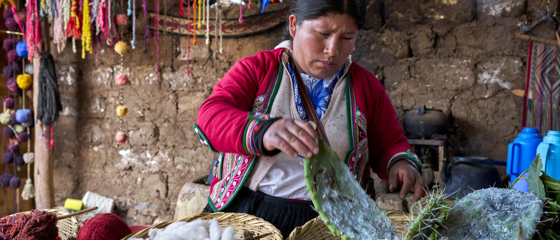 A woman works with cactus fibers and natural dyes in a craft workshop, surrounded by colorful decorations and materials.
