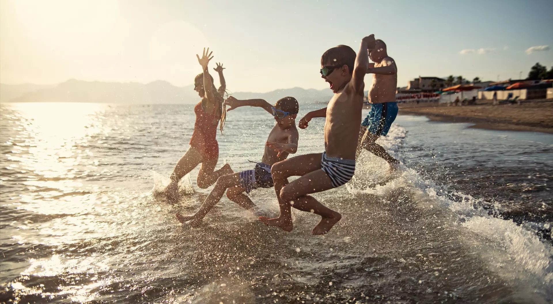 Four children splash in the water at the beach, enjoying the sunset and playing joyfully.