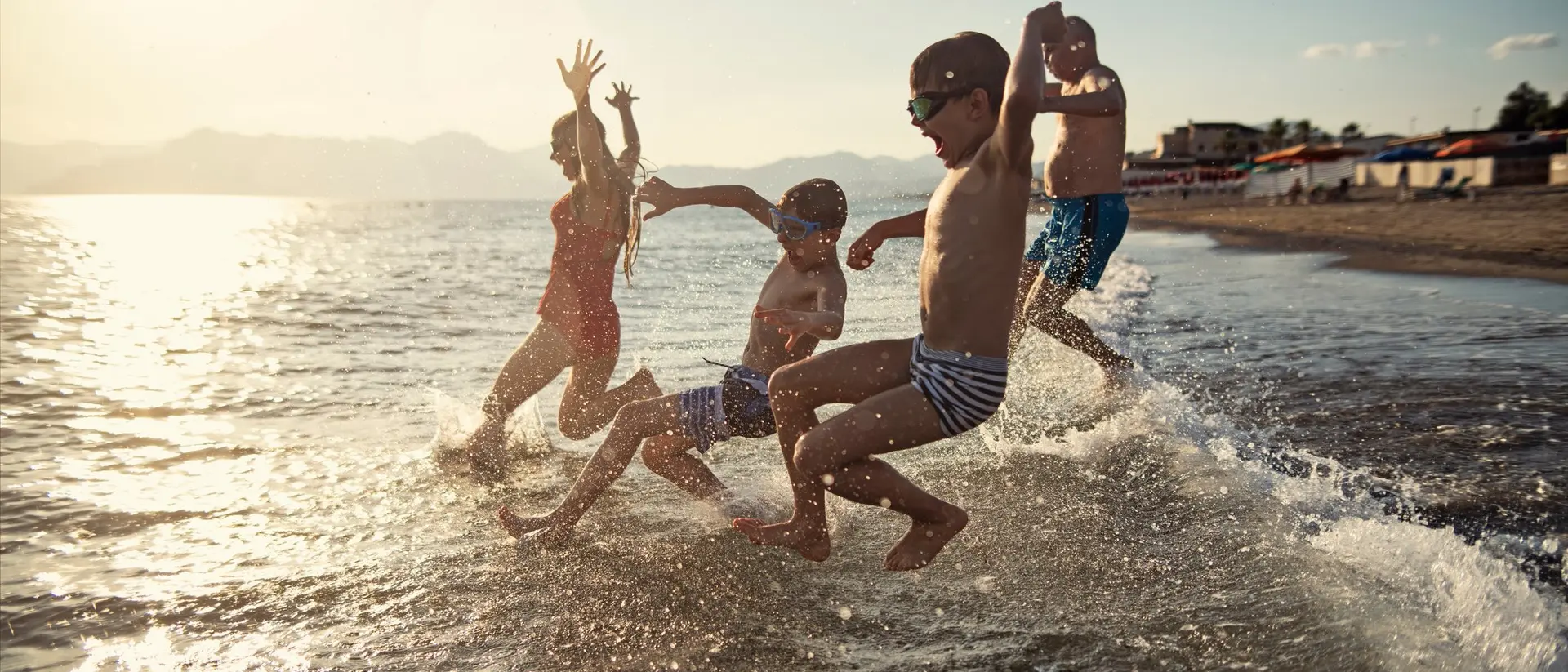Four children splash in the water at the beach, enjoying the sunset and playing joyfully.