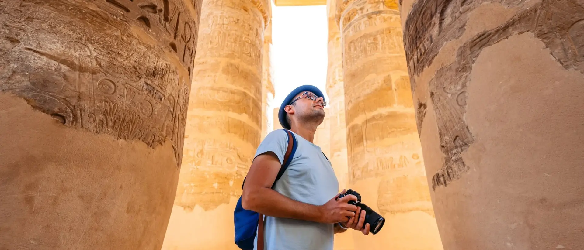 Person standing between ancient stone columns, gazing up, holding a camera
