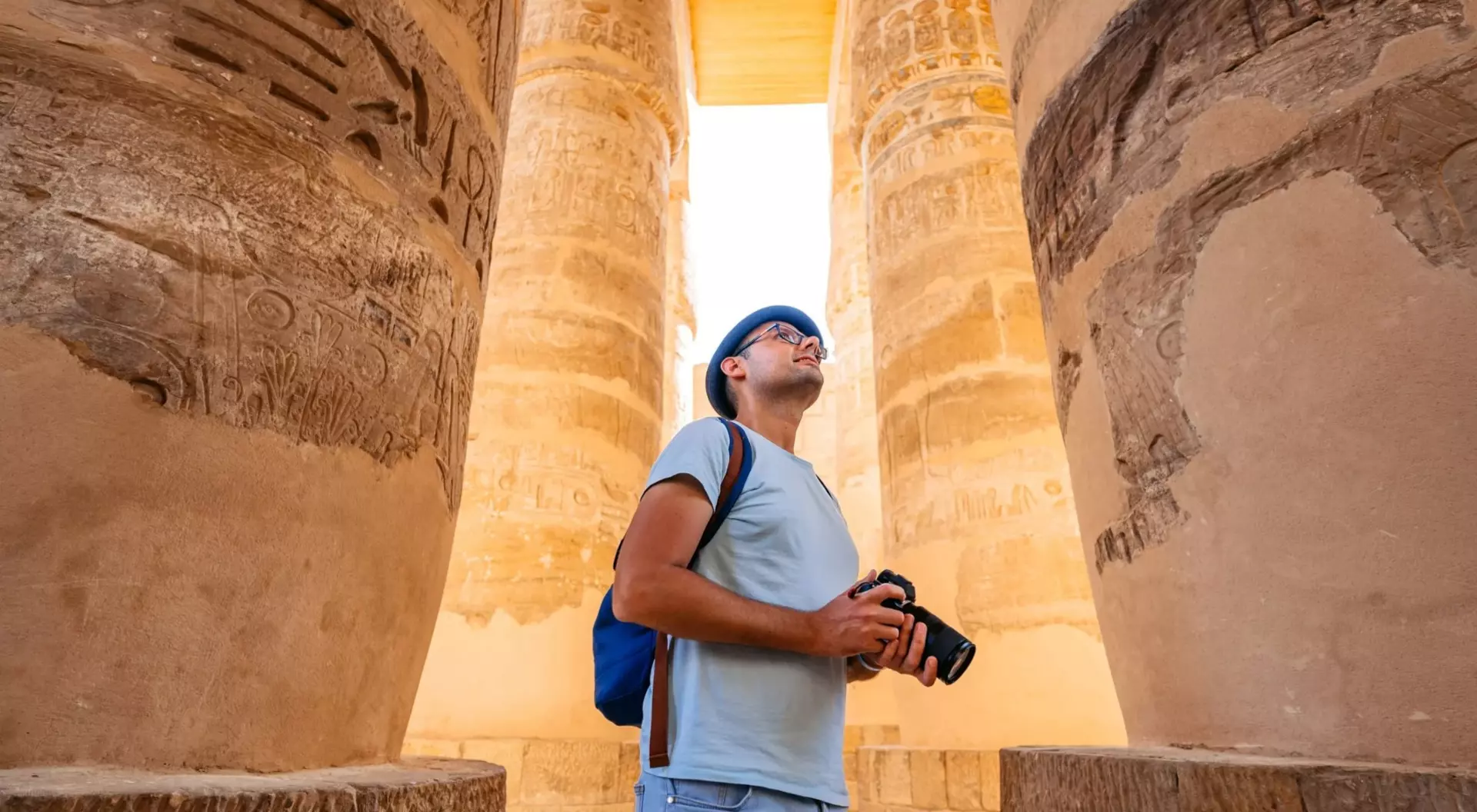 Person standing between ancient stone columns, gazing up, holding a camera