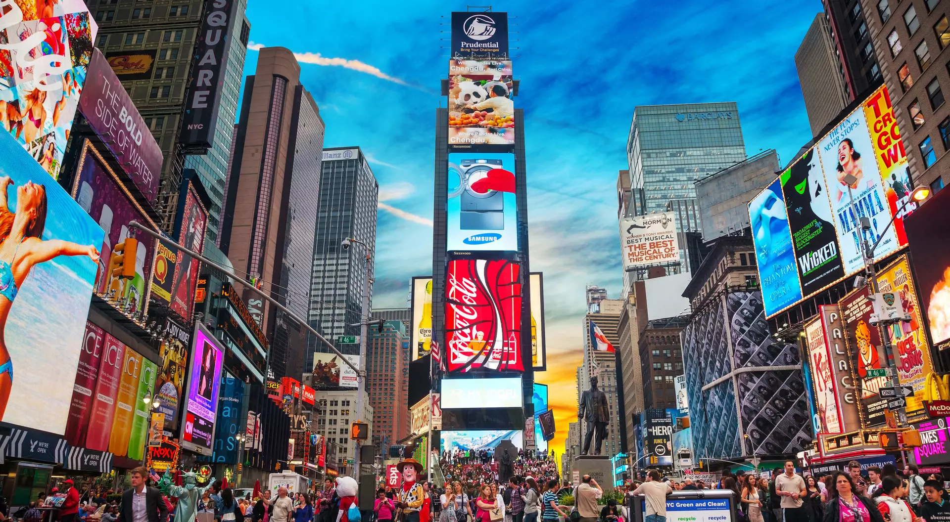 Crowds gather in Times Square, surrounded by vibrant billboards and a colorful sky at sunset.