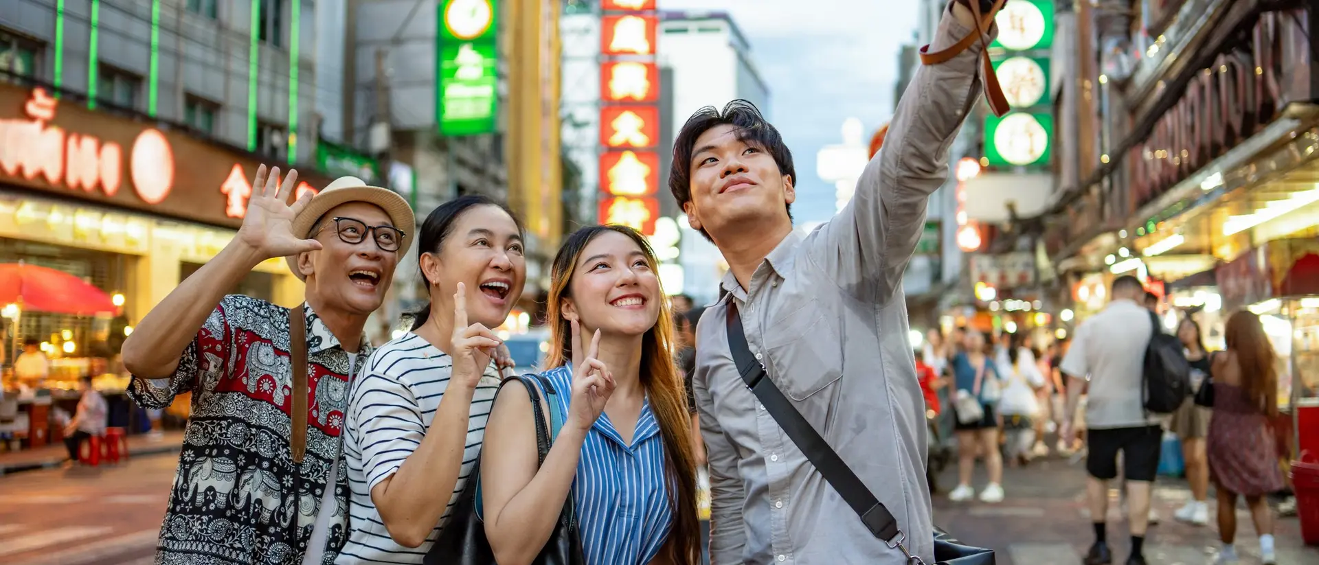 A group of four friends happily taking a selfie on a vibrant city street filled with bright signs and lights.