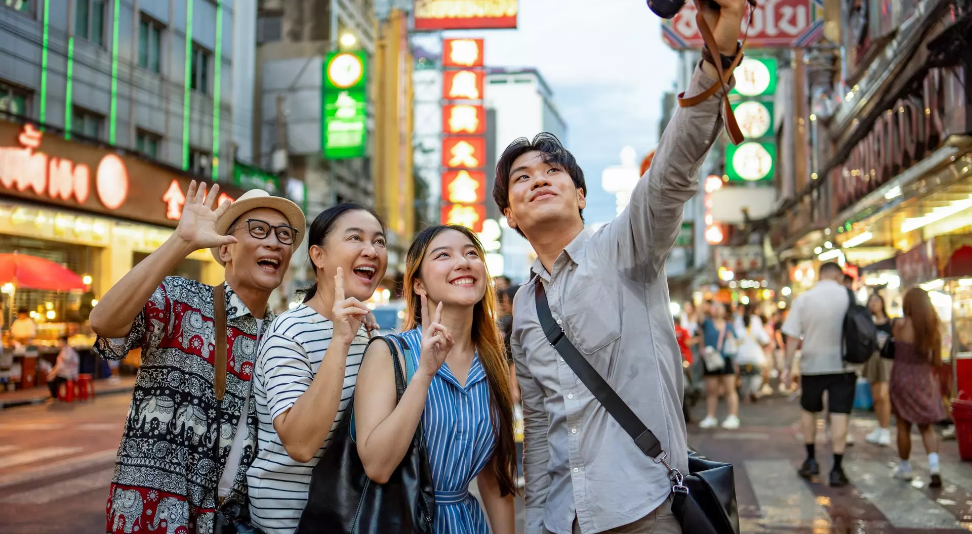 A group of four friends happily taking a selfie on a vibrant city street filled with bright signs and lights.