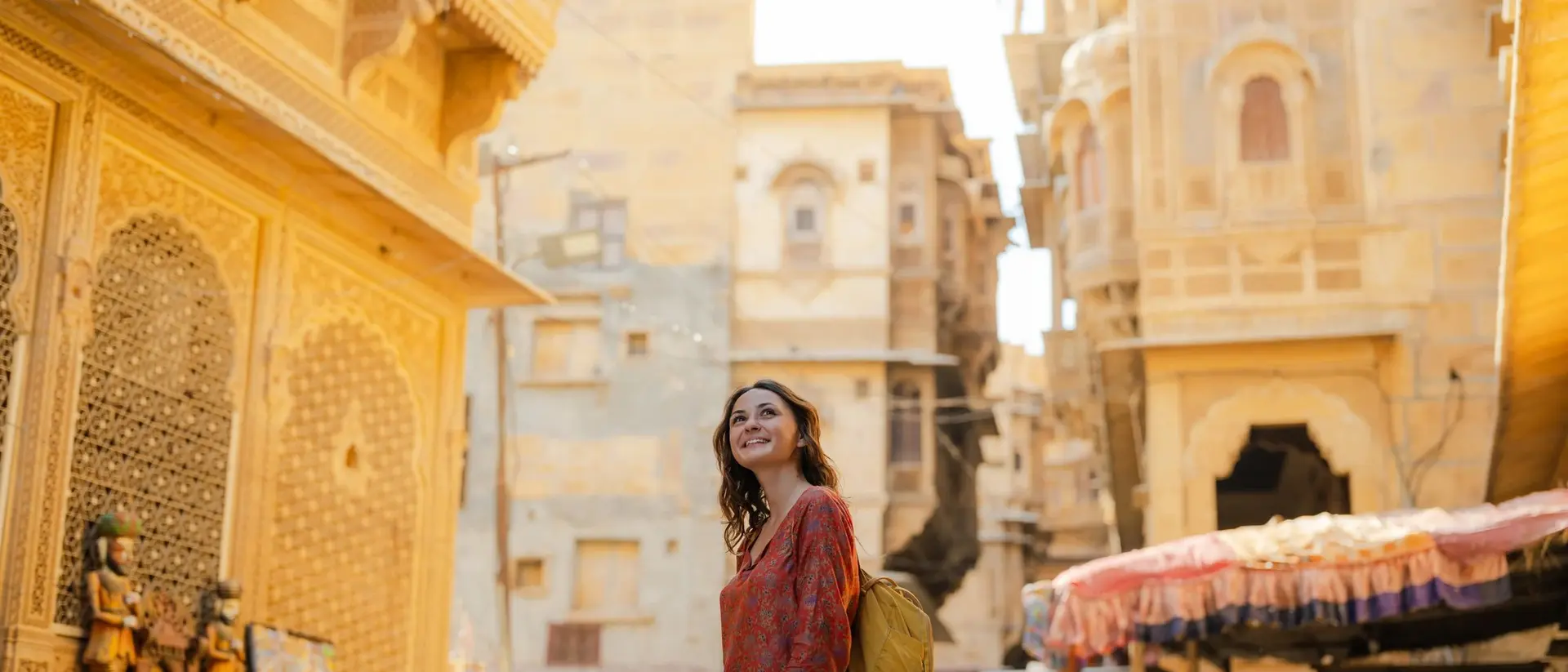 A woman in an orange dress stands in a sunlit narrow street, surrounded by historic buildings and parked motorcycles.
