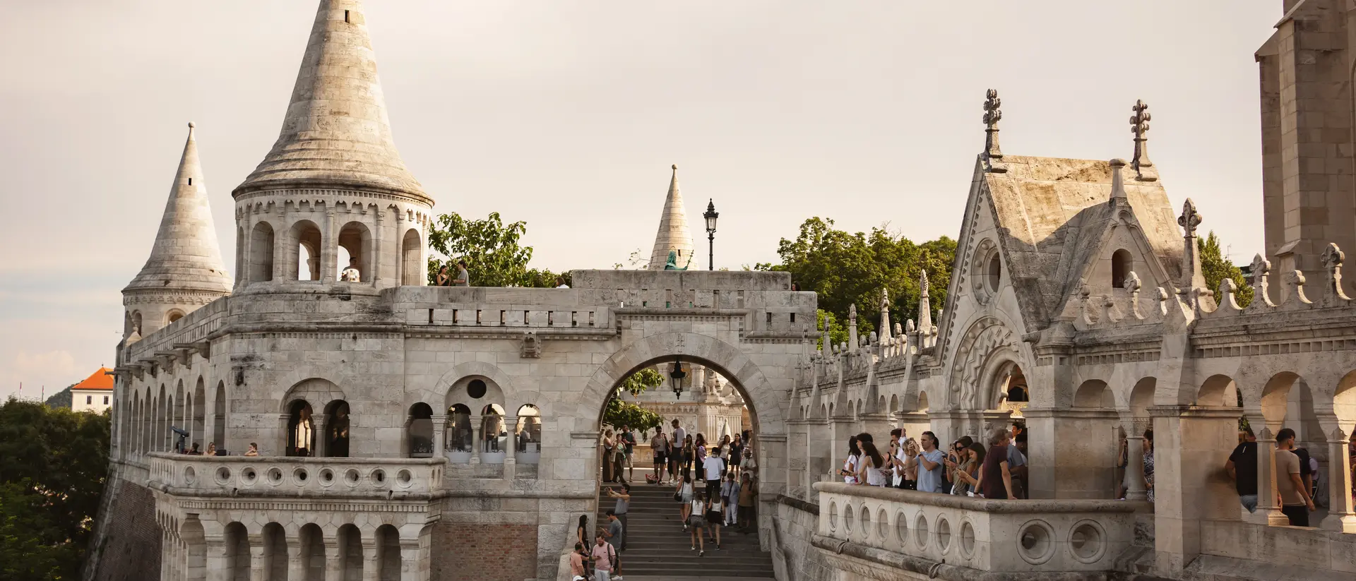 Hungarian Fisherman's Bastion with gothic towers, steps, and visitors under a cloudy sky.