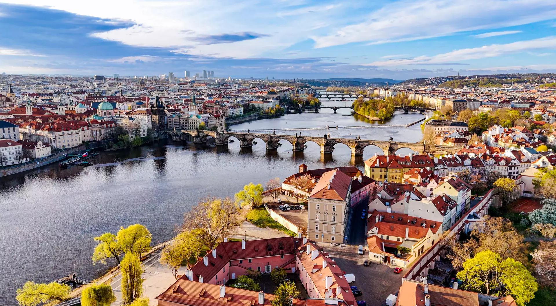 Aerial view of Prague featuring the Vltava River, bridges, and colorful buildings under a blue sky.