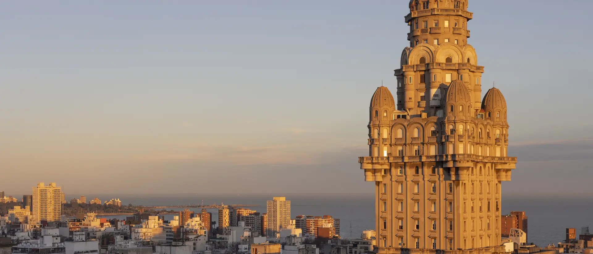 Historic tall building with intricate architecture, bathed in sunset light, overlooking a city skyline and coastline.