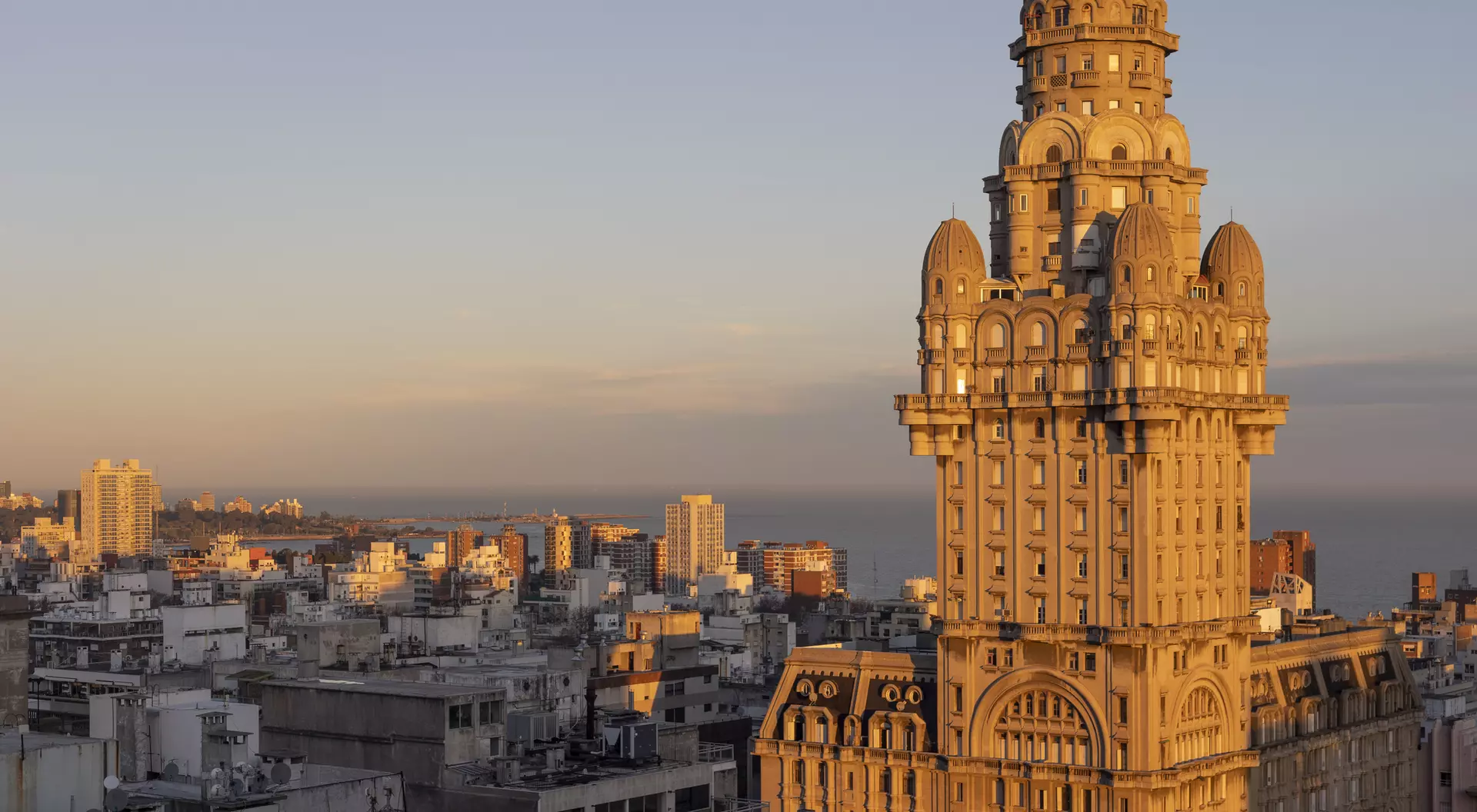 Historic tall building with intricate architecture, bathed in sunset light, overlooking a city skyline and coastline.