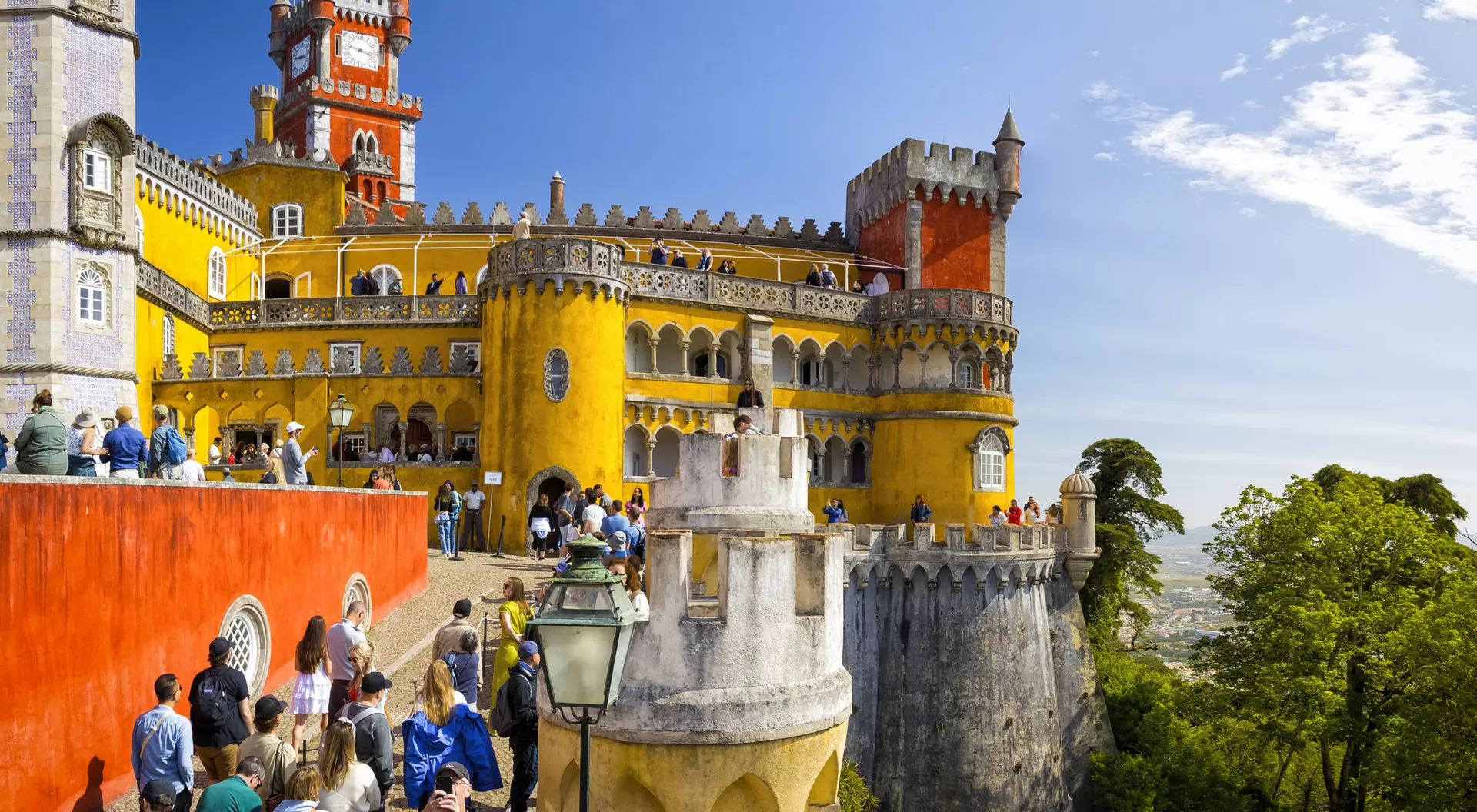 Colorful Pena Palace in Portugal, with visitors exploring its vibrant towers and scenic surroundings on a sunny day.