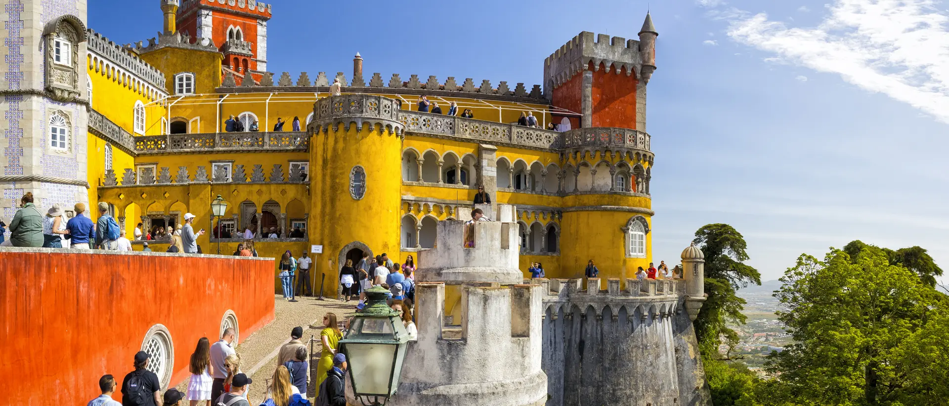 Colorful Pena Palace in Portugal, with visitors exploring its vibrant towers and scenic surroundings on a sunny day.