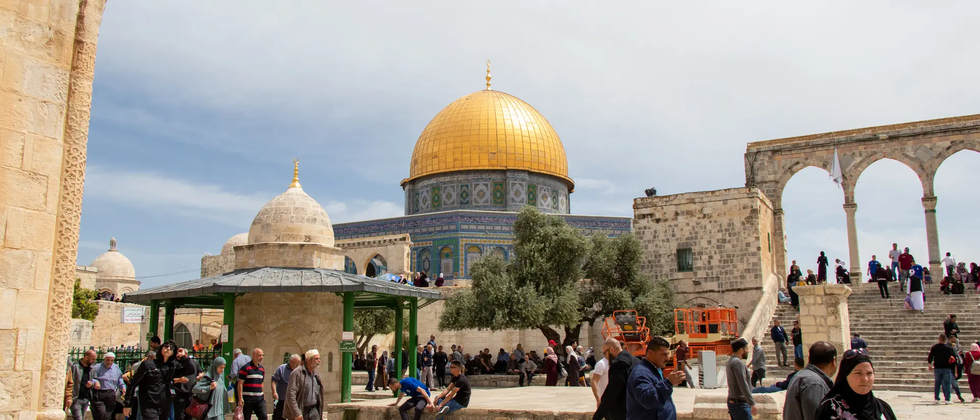 Crowds gather at the Al-Aqsa Mosque compound, featuring the iconic golden dome under a partly cloudy sky.