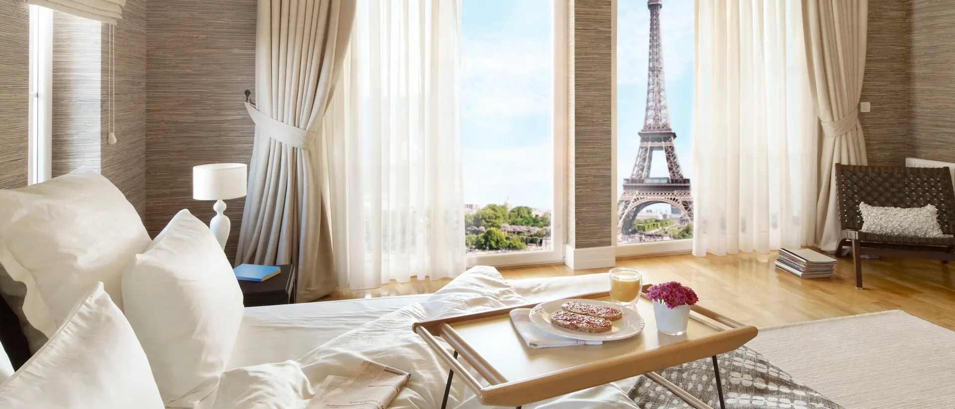 Bright bedroom with a tray on the bed, showcasing the Eiffel Tower through large windows.