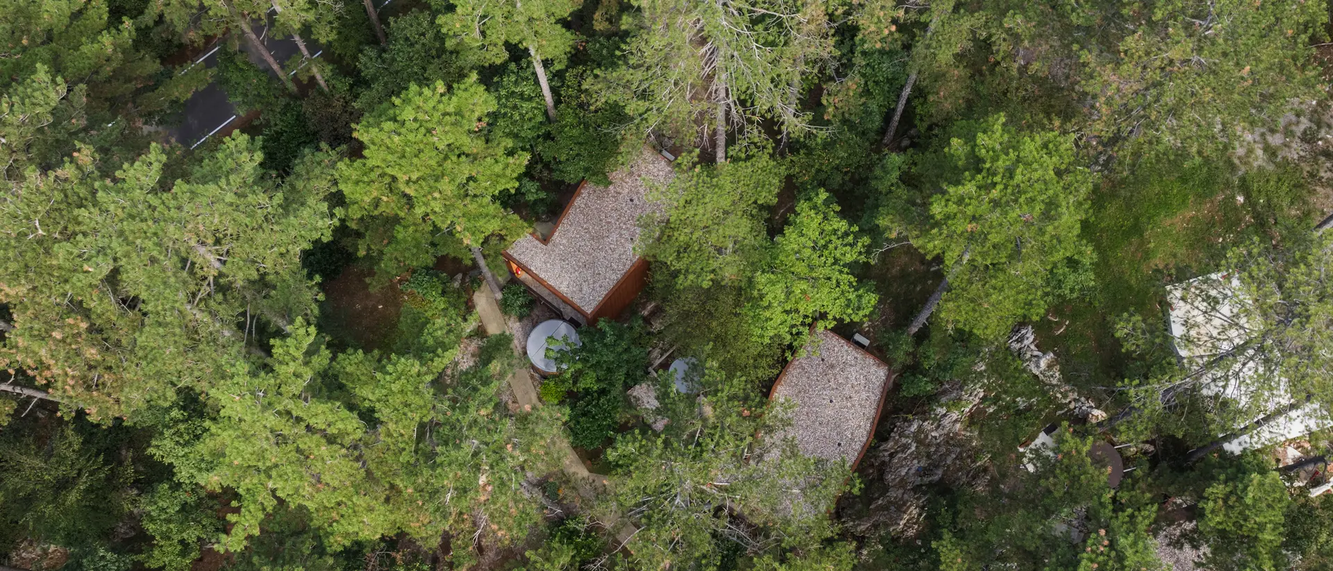Aerial view of two rustic cabins nestled among dense green trees in a forested area.