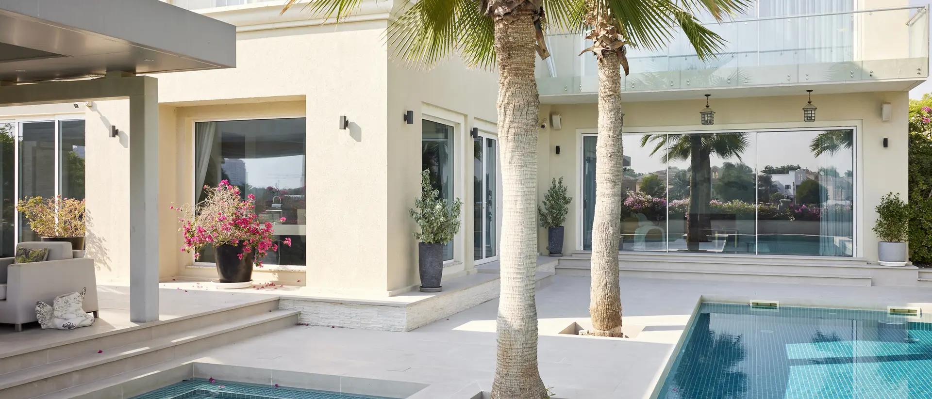 Modern villa exterior featuring a pool, palm trees, and large windows with a view of landscaped gardens.