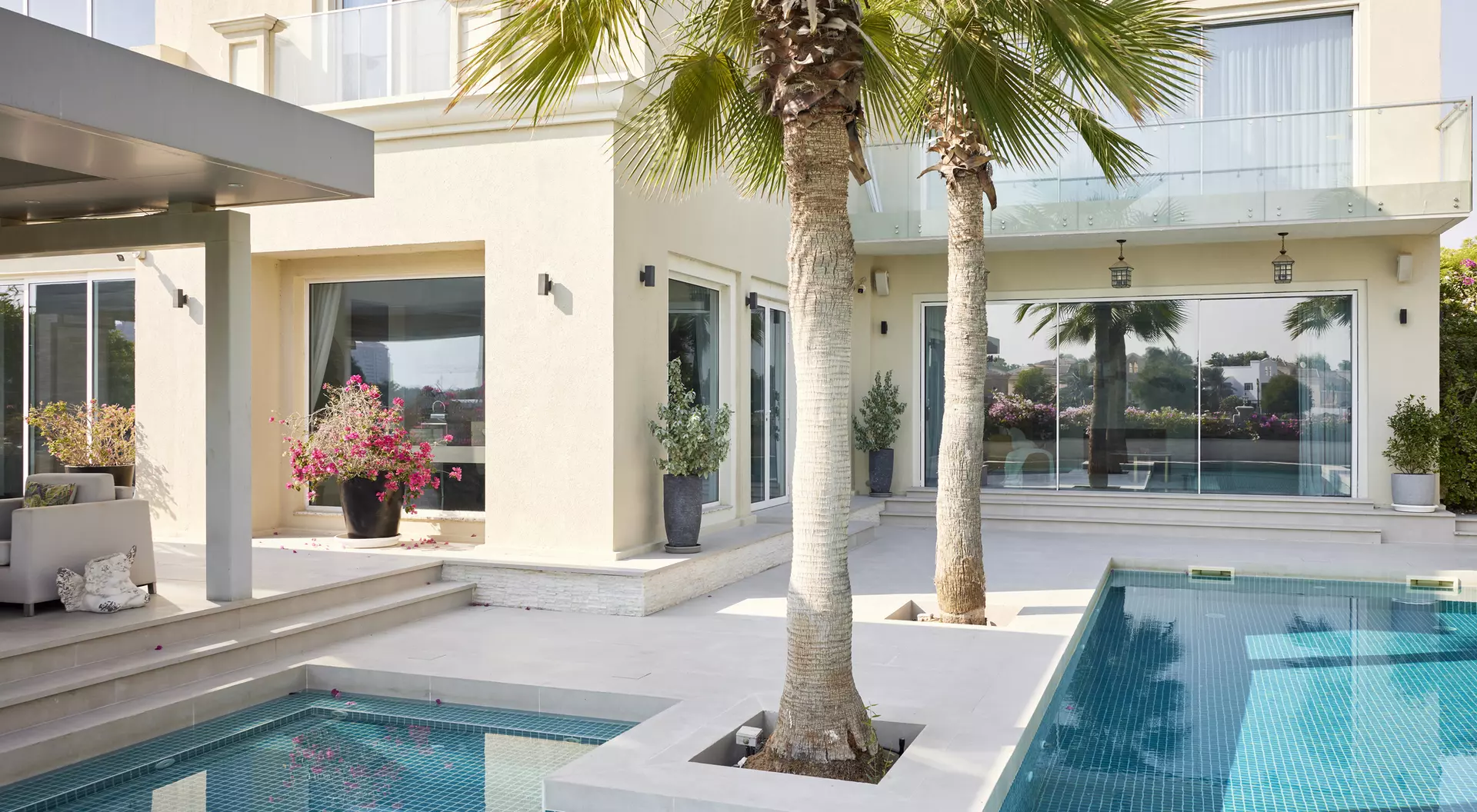 Modern villa exterior featuring a pool, palm trees, and large windows with a view of landscaped gardens.
