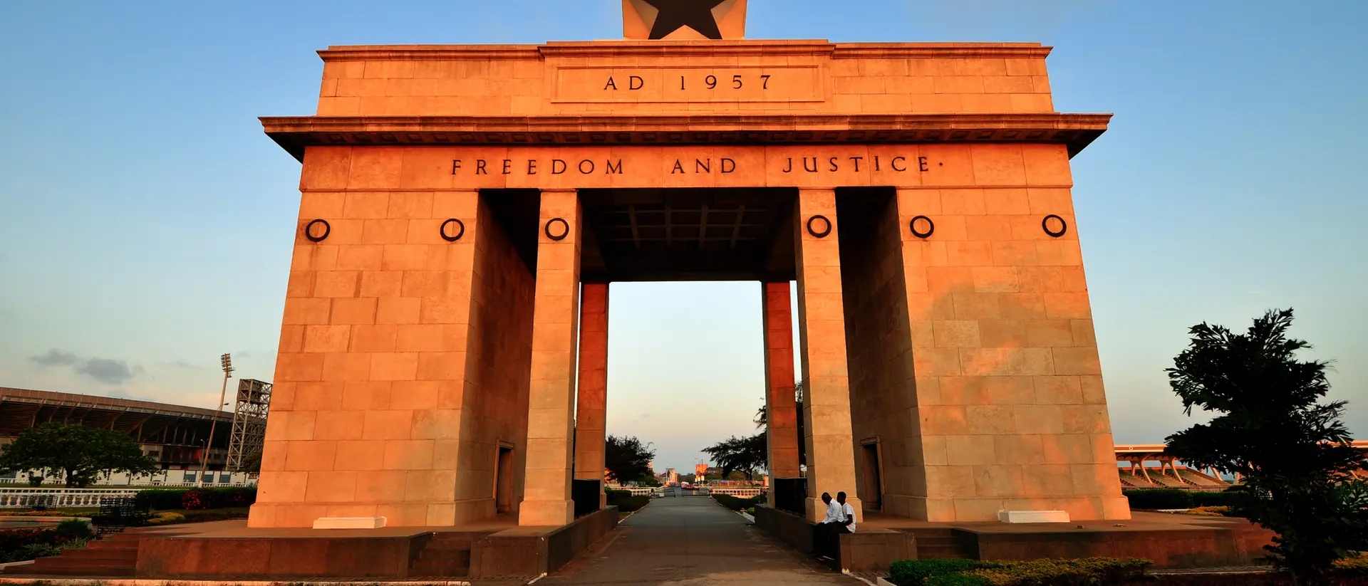 Gateway arch with a star on top, inscribed "Freedom and Justice," set in a landscaped area during sunset.