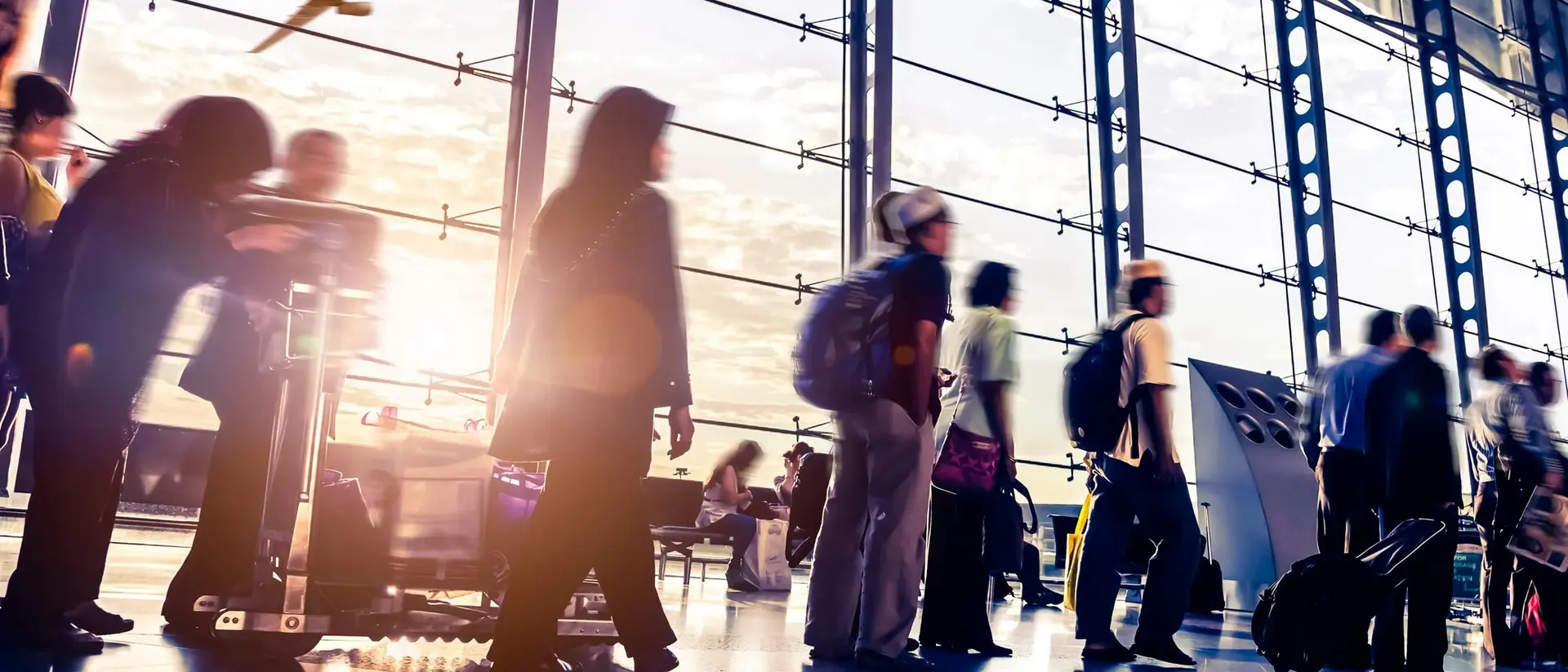Blurred travelers moving through a bustling airport terminal, with an airplane flying outside the large glass windows.