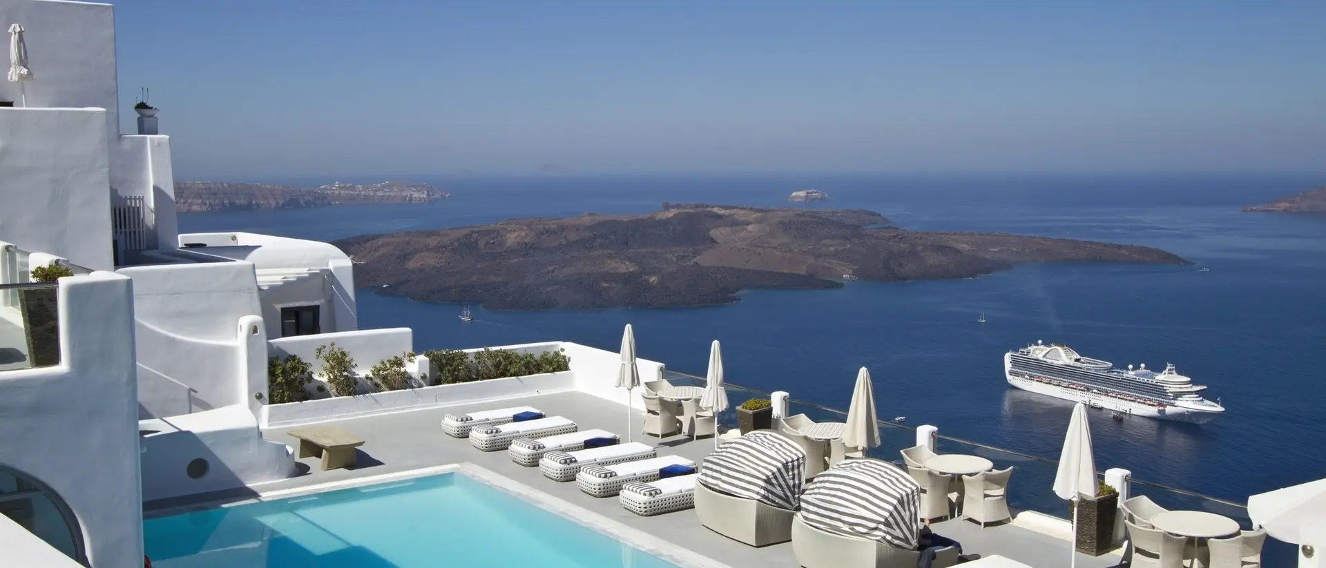 Stunning view of a pool area with lounge chairs, overlooking the ocean and islands under a clear blue sky.