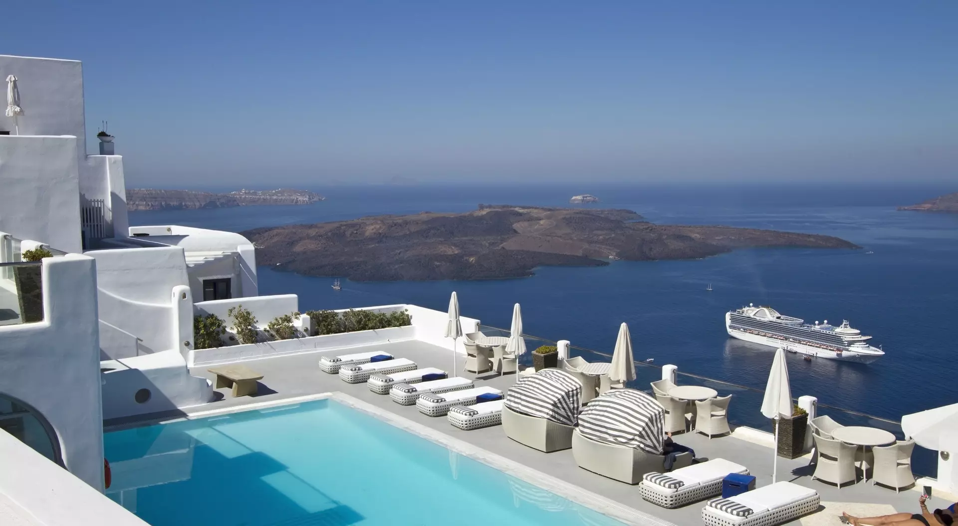 Stunning view of a pool area with lounge chairs, overlooking the ocean and islands under a clear blue sky.