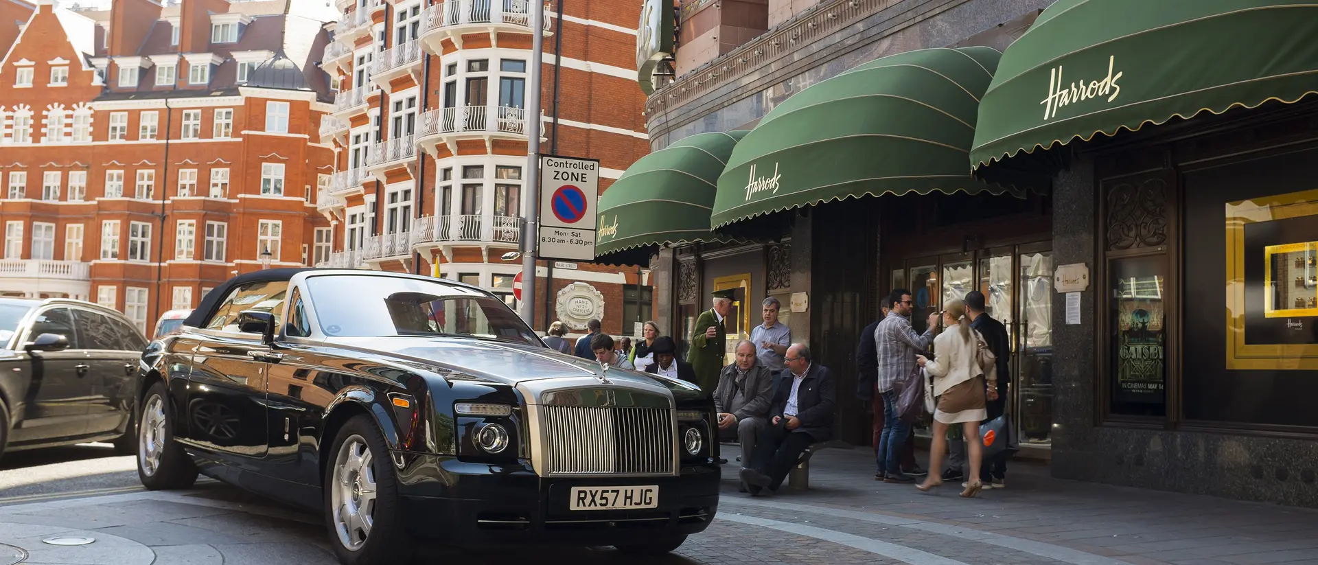 A luxury car parked outside Harrods, with people socializing nearby and a city street in the background.