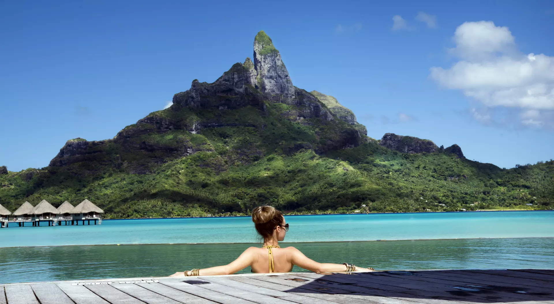 A person relaxes by the water, with a mountain in the background under a clear blue sky.