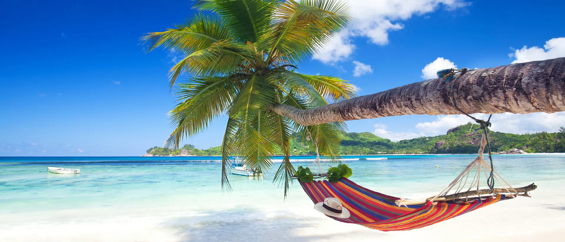 A colorful hammock hangs between palm trees over a serene beach with clear blue water and a bright sky.