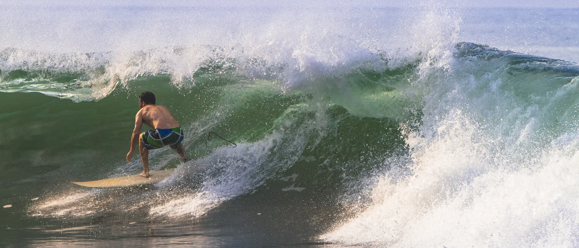A surfer rides a large wave, skillfully maneuvering on his board as the water crashes around him.