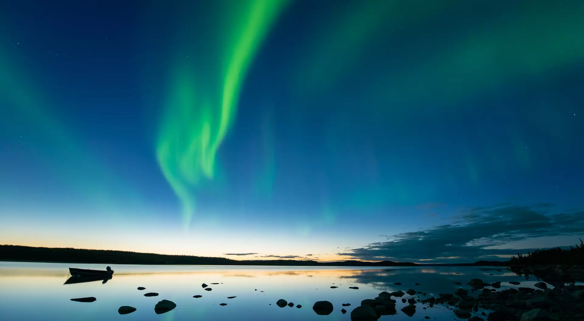 Yellowknife, Canada Bands of curvy aurora borealis appear over a northern rocky lake right after sunset.