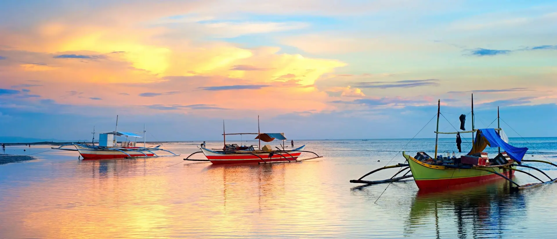 Three colorful boats on calm water under a vibrant sunset sky with clouds reflecting in the water.